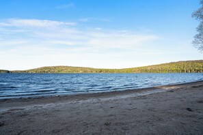 Une plage avec un ciel dégagé, une eau calme et des collines boisées en arrière-plan.