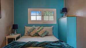 A bedroom with a bed, two pillows, a nightstand with a lamp, and a window.