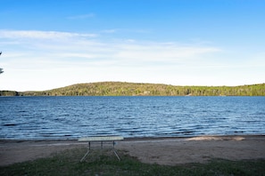 A lakeside view with a bench and a distant forested hill.