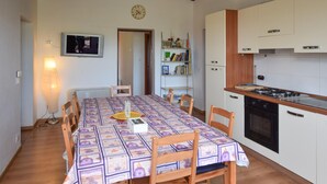 Ein Essbereich mit einem Tisch für vier Personen, eine Küche mit Herd und Backofen sowie ein Bücherregal mit verschiedenen Gegenständen.