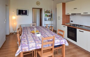 Ein Essbereich mit einem Tisch für vier Personen, eine Küche mit Herd und Backofen sowie ein Bücherregal mit verschiedenen Gegenständen.