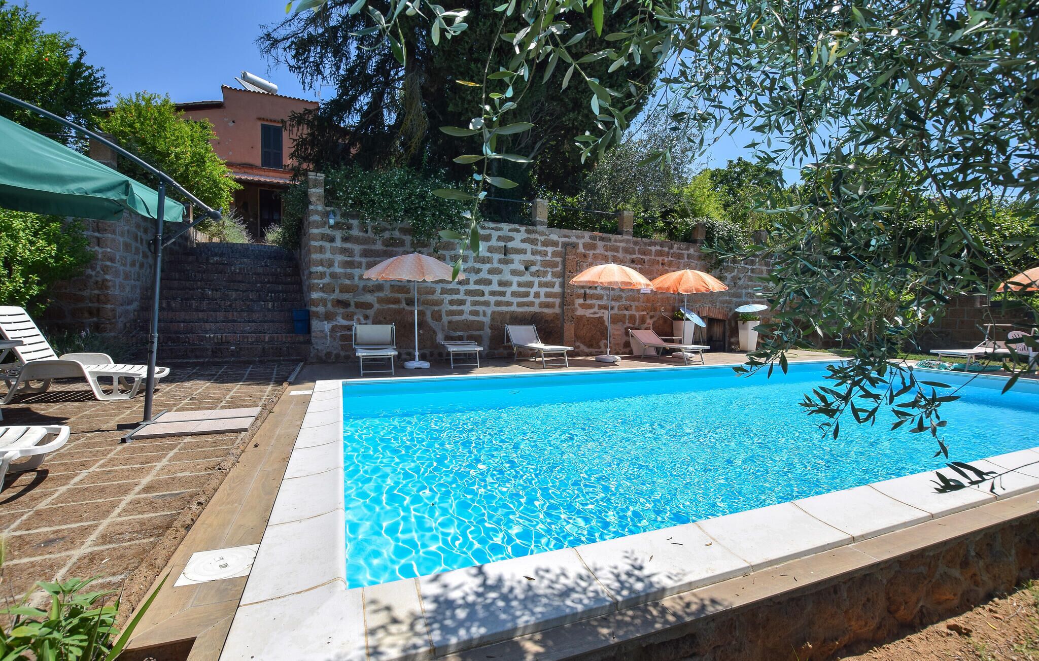 Ein Swimmingpool mit Liegestühlen und Sonnenschirmen, umgeben von Steinmauern und Grünpflanzen.