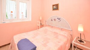 Ein Schlafzimmer mit einem Bett, einem Nachttisch, einer Lampe, einem Fenster mit Vorhängen und einem Bild an der Wand.