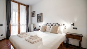 A bedroom with a bed, two wall-mounted lights, a radiator, and a window with curtains. - Italianway Easy - Corso San Gottardo 5 (Milano)