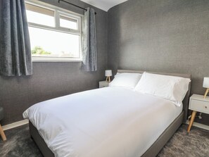 Ein Schlafzimmer mit einem großen Bett, grauen Wänden, einem Fenster mit Vorhängen und Nachttischen mit Lampen.