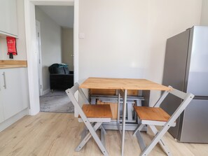 Una cocina compacta con una mesa de madera, dos sillas, un refrigerador y una manta anti-fuego en la pared.
