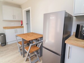 Eine kompakte Küche mit einem Edelstahl-Kühlschrank, einem Holztisch und weißen Schränken.