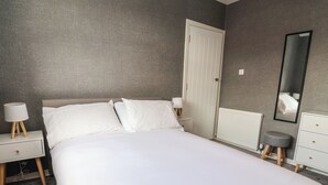 Ein Schlafzimmer mit einem Bett, Nachttischen, einer Kommode, einem Spiegel und einer Tür.