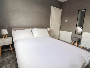 Um quarto com cama, mesas de cabeceira, penteadeira, espelho e uma porta.