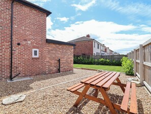 A brick building with a gravel patio and a wooden picnic table.