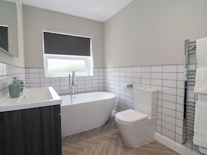 Ein modernes Badezimmer mit einer freistehenden Badewanne, einer Toilette und einem Fenster.