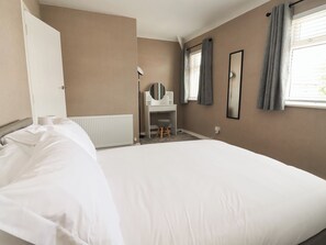 Ein Schlafzimmer mit Bett, Schreibtisch, Stuhl, Heizkörper, einem fenster mit Vorhängen und einem Spiegel an der Wand.
