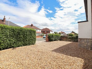 Uma entrada de garagem residencial com cascalho, um hedge e casas ao fundo.