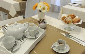 Ontbijt met een theepot, kopjes, een dienblad, een vaas met bloemen en een bord gebak.