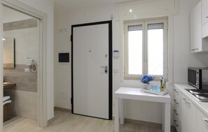 Ein Hotelzimmer mit Badezimmer, einem weißen Schreibtisch mit einer Vase, einer Mikrowelle und einem Fenster mit Jalousien.