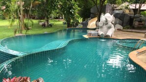 Ein Schwimmbecken mit gefliestem Rand, einer Holzterrasse und einem Wasserfall.