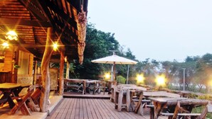 Eine Holzterrasse mit Tischen und Bänken, ein überdachter Sitzbereich und ein Gebäude im rustikalen Stil.