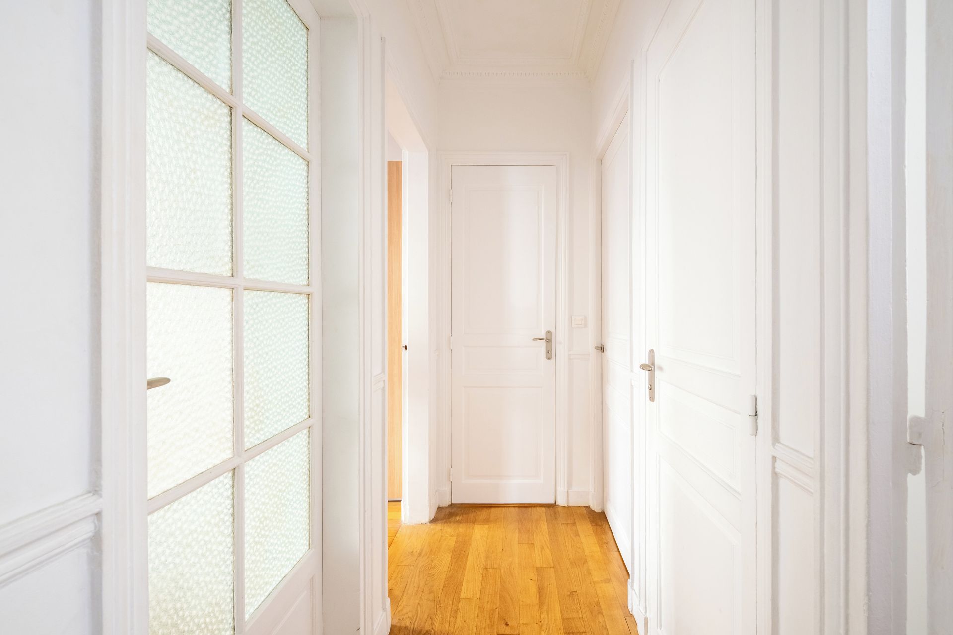 Un pasillo con puertas blancas y suelo de madera.