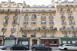 A multi-story building with balconies, a storefront, and parked cars. - Charming 1BDR Apartment for 3 Near Eiffel Tower (Paris)