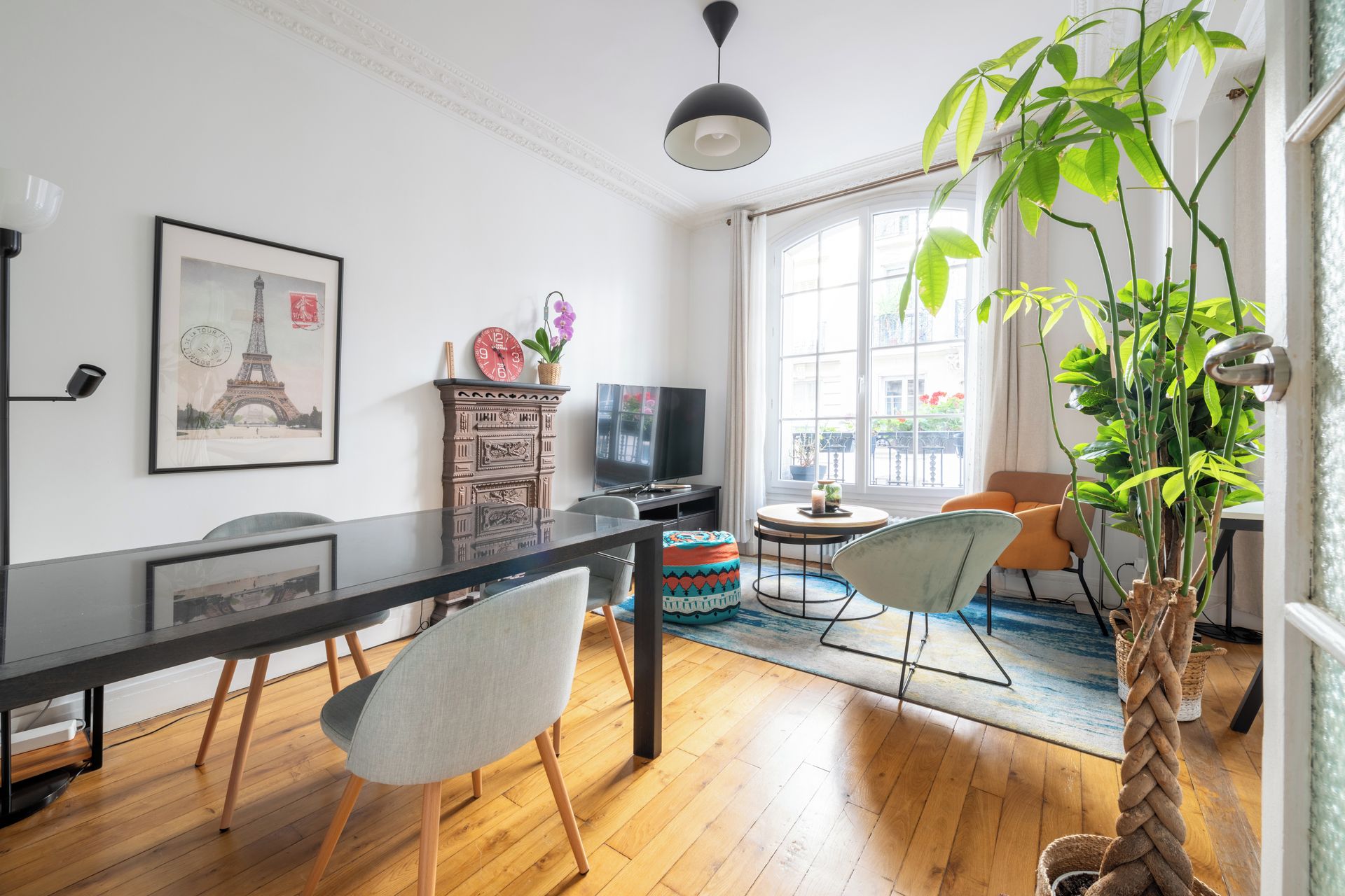 A modern living room with a dining table, chairs, a television, and a large window.