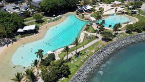 Vista aérea de um resort com uma grande piscina, área de praia e costa rochosa.