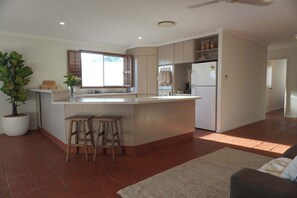 A modern kitchen with a central island, wooden stools, a potted plant, and a refrigerator. - The Balcony at Airlie (Airlie Beach)