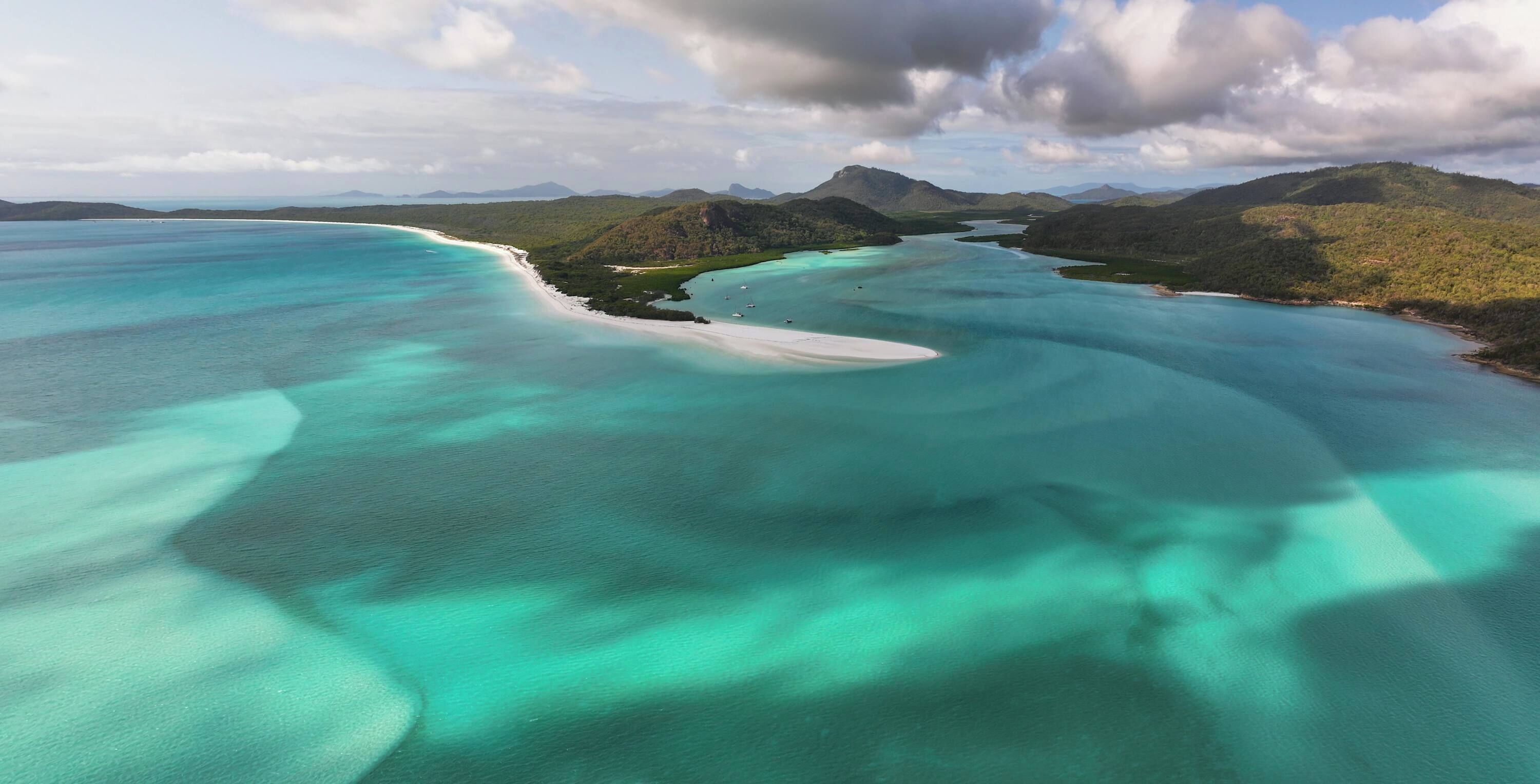 A coastal landscape with clear turquoise waters, white sandy beaches, and green hills.