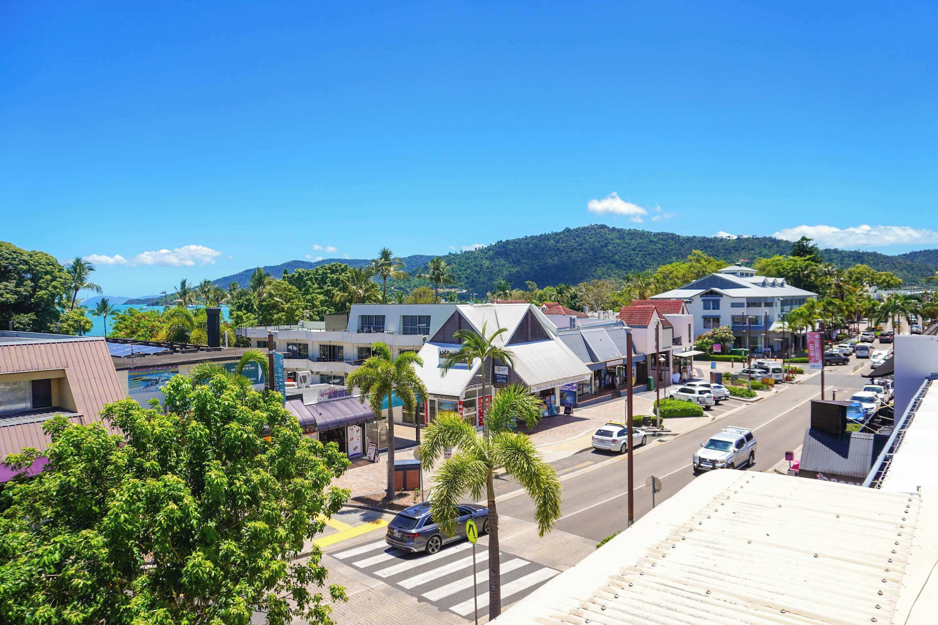A coastal town with buildings, a street, and palm trees.