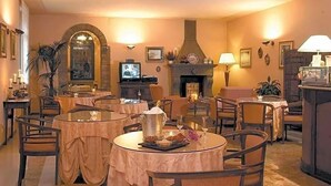 Un'area ristorazione d'hotel con tavoli rotondi, sedie, un caminetto e un televisore.