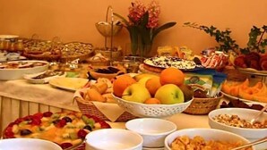 A buffet table with various food items and a vase of flowers. - Hotel Castello (Modena)