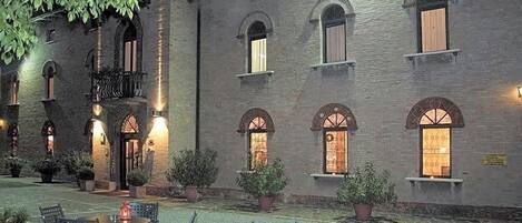 A courtyard with outdoor seating, a brick building with arched windows, and potted plants.