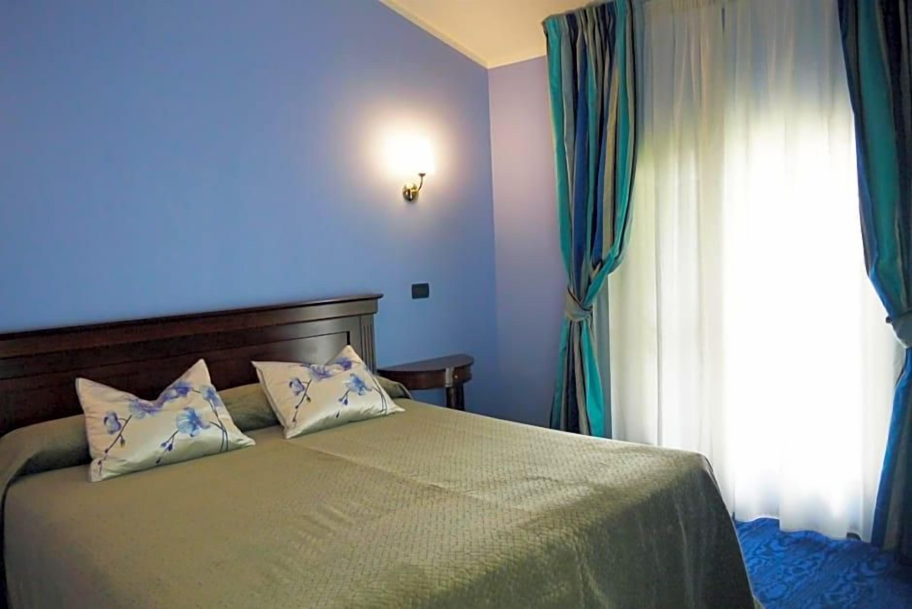Un lit avec une tête de lit, deux oreillers, une table de chevet et un luminaire fixé au mur.