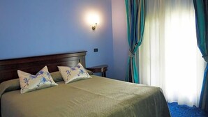 A bed with a headboard, two pillows, a bedside table, and a wall-mounted light fixture. - Hotel Castello (Modena)
