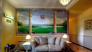 Una hall con un divano, due lampade, un quadro raffigurante un paesaggio e un lampadario.
