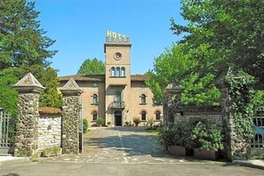 A historic building with a central tower, a stone entrance gate, and a paved driveway leading to the entrance. - Hotel Castello (Modena)