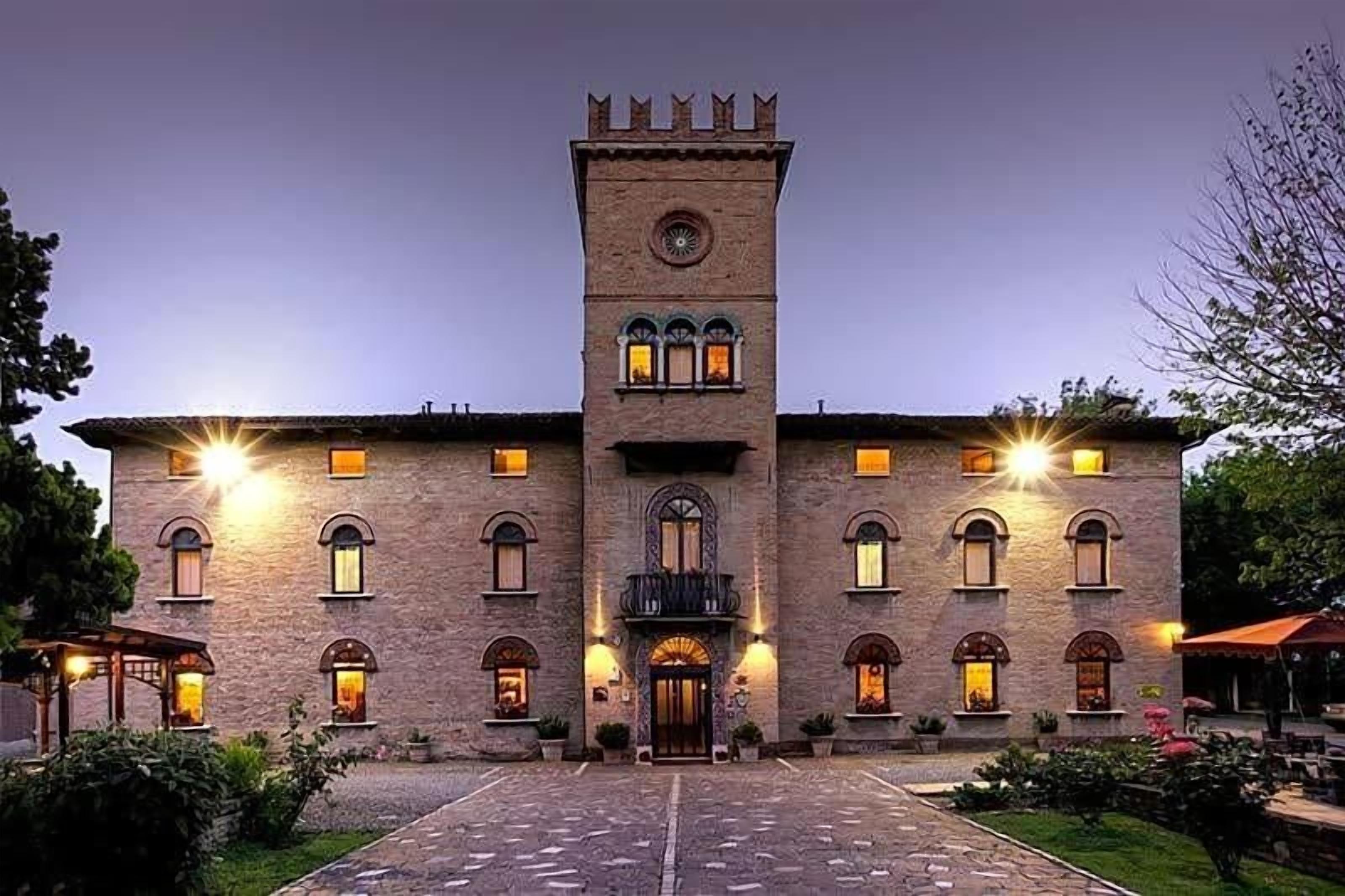 Un edificio grande e storico con una torre centrale, numerose finestre e un’area d’ingresso pavimentata.
