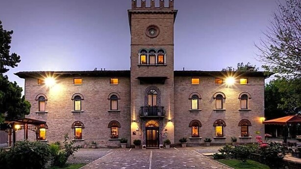 Un edificio grande e storico con una torre centrale, numerose finestre e un’area d’ingresso pavimentata.