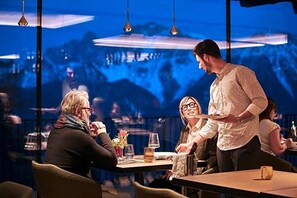 A restaurant with tables, chairs, and hanging lights. - Olangerhof Hotel Spa (Valdaora)
