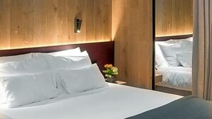A modern hotel room with a large bed, wooden panel walls, a nightstand, and a mirror. - Olangerhof Hotel Spa (Valdaora)