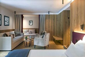A modern hotel room with a sofa, armchair, and a bed. - Olangerhof Hotel Spa (Valdaora)