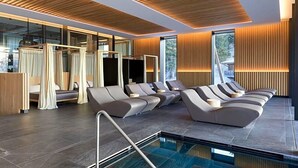 A modern spa area with a pool, reclining chairs, and a wooden ceiling. - Olangerhof Hotel Spa (Valdaora)