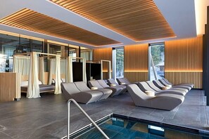 A modern spa area with a pool, reclining chairs, and a wooden ceiling. - Olangerhof Hotel Spa (Valdaora)