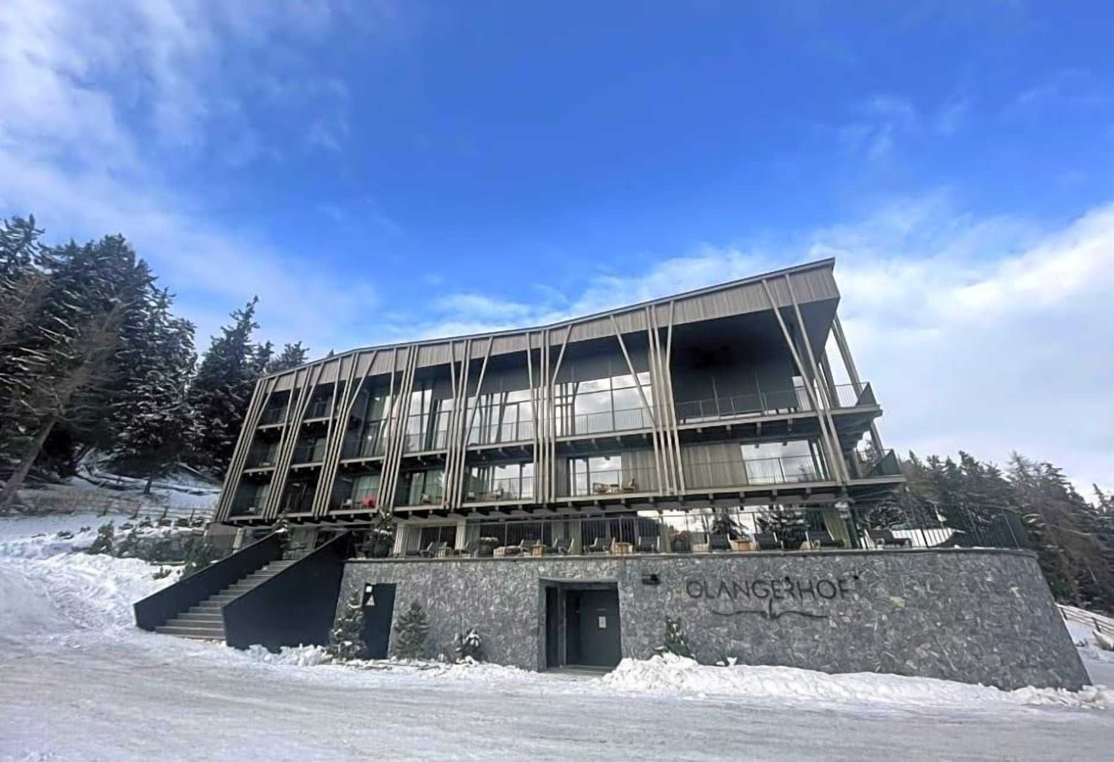 Un bâtiment moderne doté d’une façade en verre, d’un socle en pierre et d’un escalier menant à l’entrée.