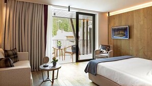 Ein Hotelzimmer mit Bett, einer Sitzecke, einem kleinen Tisch mit Pflanze, einem Sessel und einem Balkon mit Aussicht.