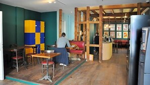 A restaurant interior with wooden tables, chairs, a counter, and a person seated at a table. - Hostel 20 Bayonne (Bayonne)