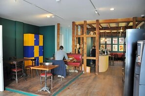 En restaurantindretning med træborde, stole, en disk og en person siddende ved et bord.