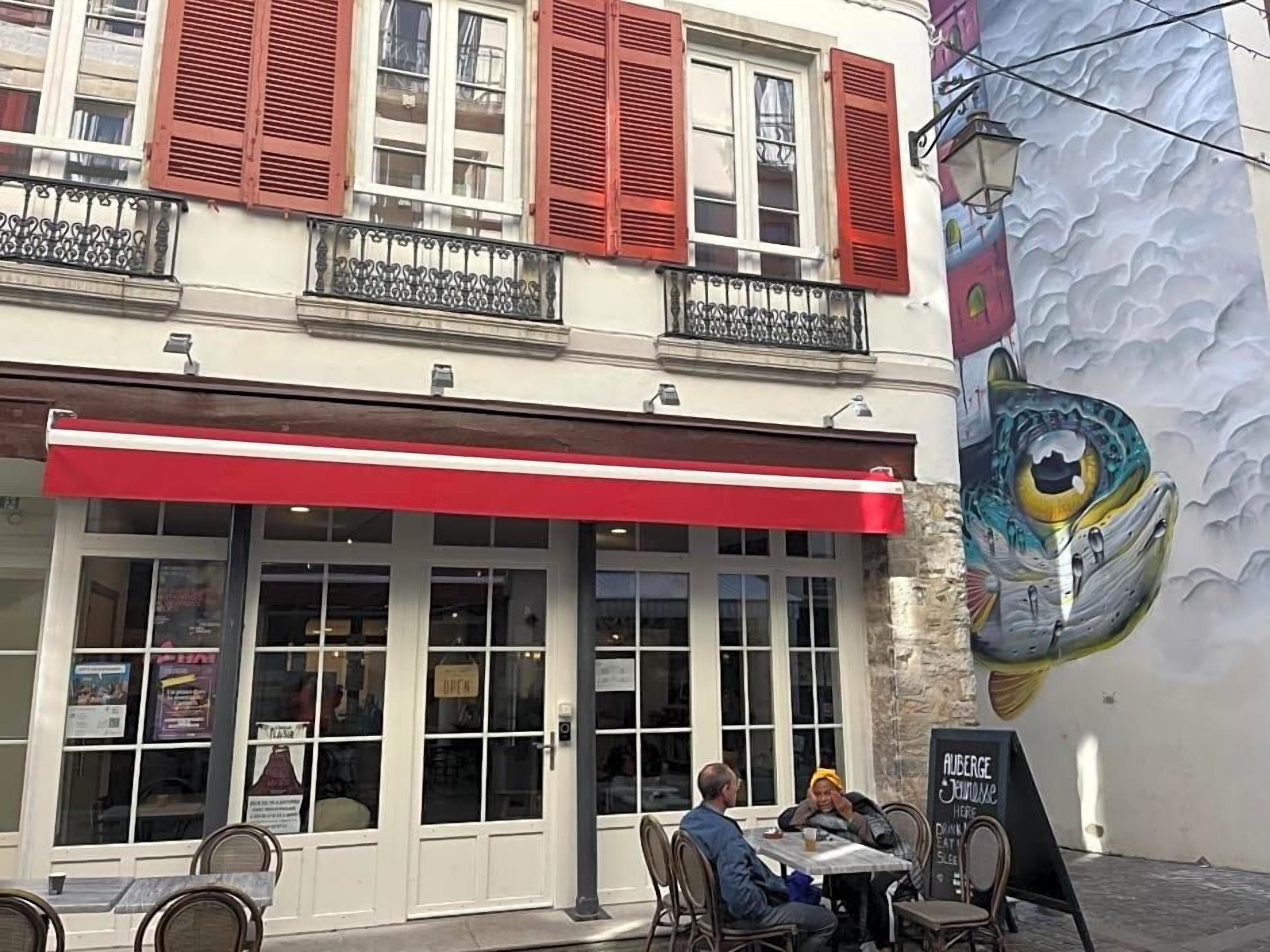 Un restaurant avec une terrasse, un auvent rouge et une fresque murale.