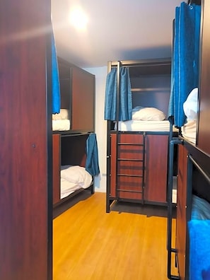 Un dormitorio con literas, suelo de madera, una escalera y cortinas.