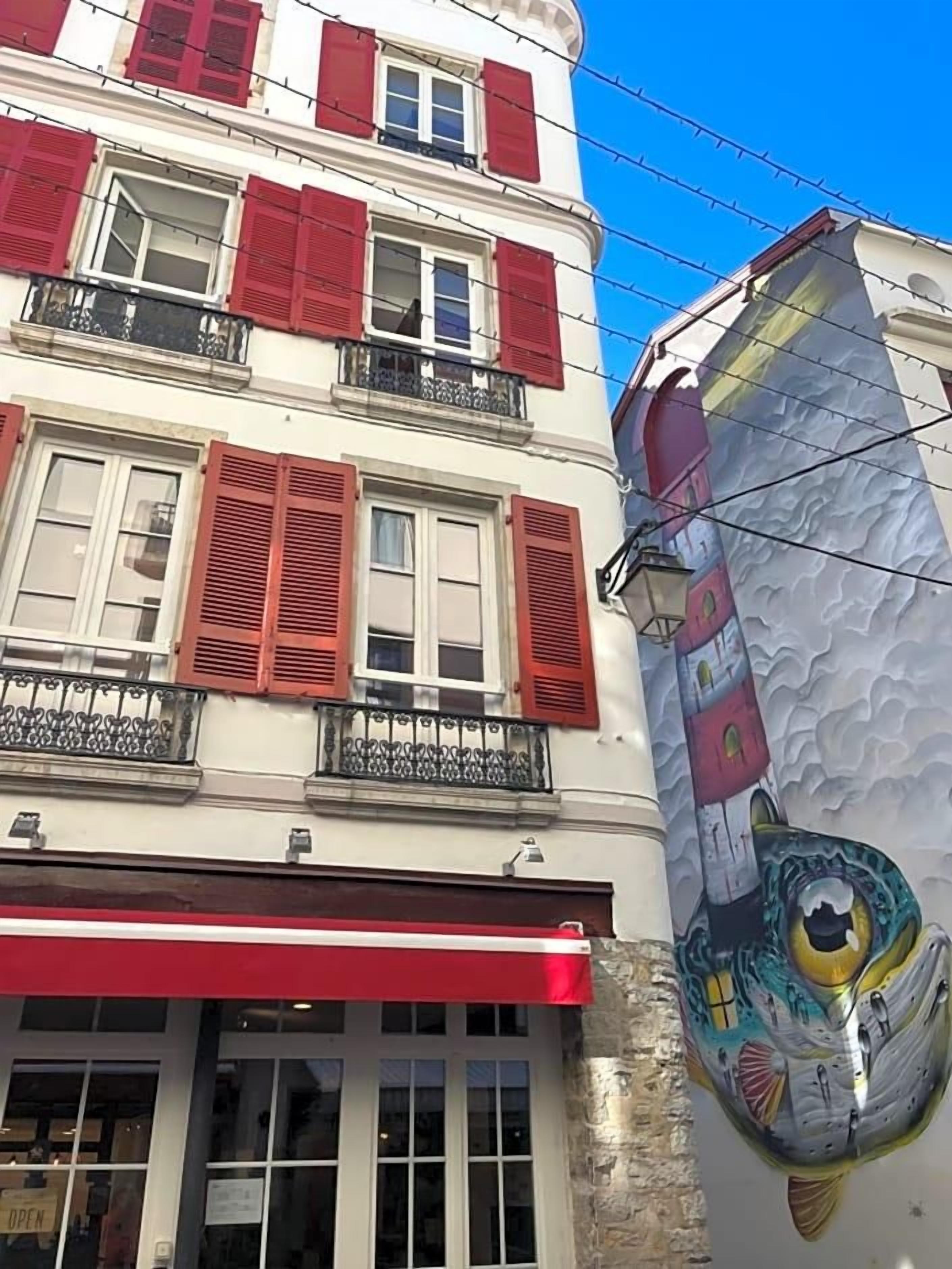 En bygning med røde skodder, en balkon og et stort muralmaleri.