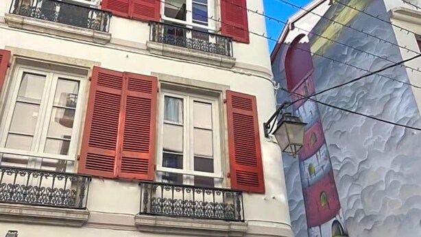 A building with red shutters, a balcony, and a large mural. - Hostel 20 Bayonne (Bayonne)